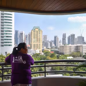 A woman in a purple shirt looks out over the skyline of Bangkok.