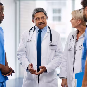 An older physician in a white coat talking to colleagues