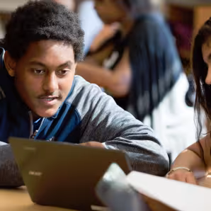 Image of two students in a classroom, one with a laptop