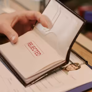 Image of a hand holding a passport with the stamp 'rejected' on a passport page