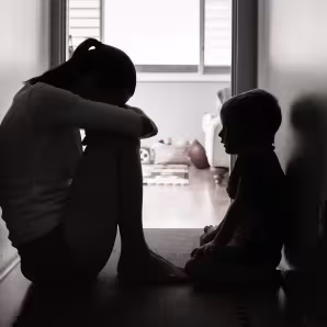 A sad mother and child sit in a dark hallway.