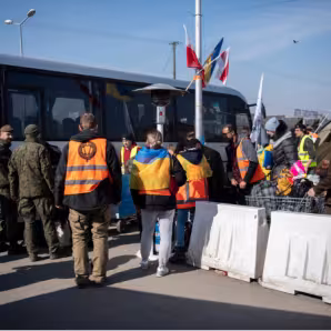 Ukrainian refugees and military members stand near a bus in Poland. 