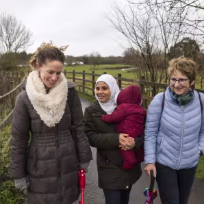 Three women, one in a headscarf and holding a baby, walk in the countryside in Devon, UK
