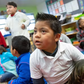 A prekindergarten student sitting on the floor with classmates