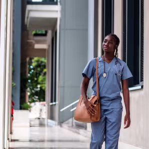 A Black female nurse in blue scrubs walking outside