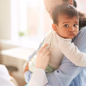 Mother holds her young child while doctor examines him with a stethoscope