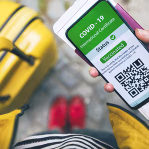 Woman holding a passport and mobile phone with a vaccine credential app in her right hand and yellow