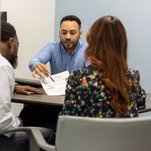 Three people sit at a desk and discuss a form