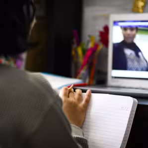 A girl sits facing a laptop, where she watches her teacher as part of virtual classes during the COVID-19 pandemic