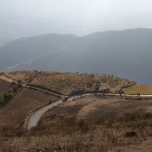 A road cuts across mountains and hills, with clouds in the background, in Huehuetenango, Guatemala