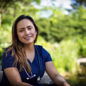 A young female nurse wearing medical scrubs and a stethoscope sits on a park bench