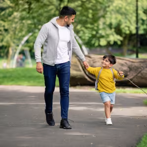 A young boy holds hands with his dad as they walk in a park
