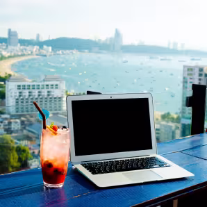 A laptop and cocktail on a ledge overlooking the beach