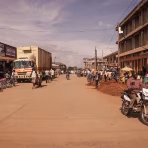 Motorcyclists and pedestrians travel a road between buildings in Arua, Uganda