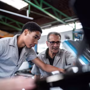 Auto mechanics, one young and one old, look at a car engine in a repair shop