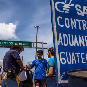 Two men and a young woman standing next to the Guatemala-Mexico border