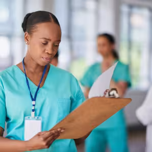 A woman wearing scrubs in a health-care setting reviews a chart