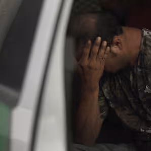 An apprehended migrant sits in a truck with his hands in his face