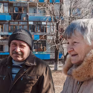 An older man and woman stand in front of an apartment building