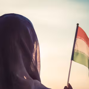 A woman holding an Iranian flag at sunset.