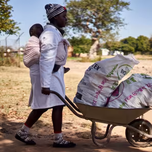 A woman in Zimbabwe pushes a wheelbarrow.