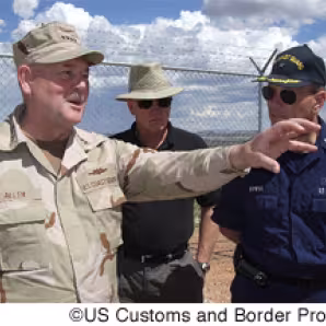 Officials from the Coast Guard and Border Patrol meet along a stretch of SBI fence in Arizona.