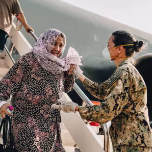 A U.S. service member helps an older Afghan woman off a plane at a naval air station