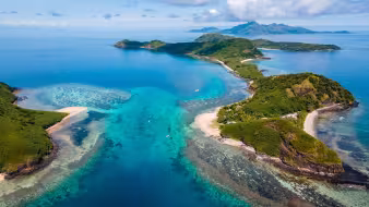 Aerial view of the Mamanuca Islands, with lush green islands, white-sand beaches, and vivid turquoise coral reefs stretching into deep blue water