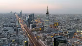 Aerial dusk view of Riyadh along King Fahd Road, with the pyramid-shaped Al-Faisaliah Tower in the foreground and Kingdom Centre Tower in the distance