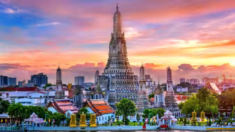 Wat Arun, the Temple of Dawn, with its towering ornate prang reflected on the Chao Phraya River in Bangkok at sunset