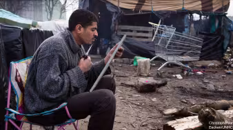 An asylum seeker trims his beard in a mirror on his lap