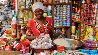 A woman at a stall smiles behind a counter full of goods for sale.