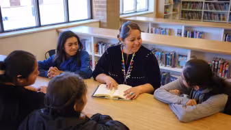  A high school teacher and students sit around a table in a school library