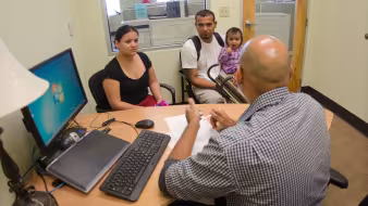 A couple and a young child talk to a man behind a desk