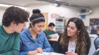 A teacher helps two high school students at their desks
