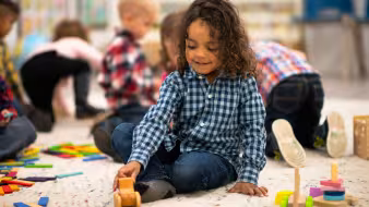 Young child seated on floor in classroom playing with a toy