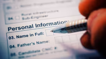 A pen poised above a form reading "Personal Information: Name in Full"