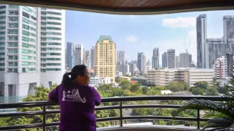 A woman in a purple shirt looks out over the skyline of Bangkok.