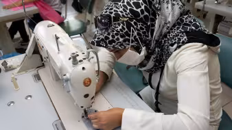 A woman in a headscarf leaning over a sewing machine.