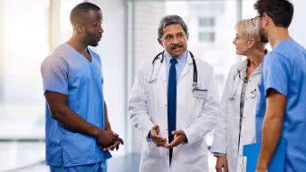 An older physician in a white coat talking to colleagues