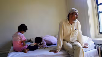 Bhutanese refugee sits on bed in family's apartment in New York
