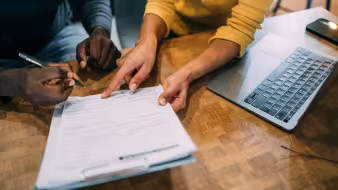 Image of the hands of two people at a desk going over paperwork