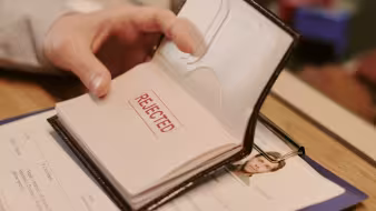 Image of a hand holding a passport with the stamp 'rejected' on a passport page