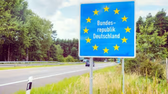 A German border sign next to a road