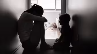 A sad mother and child sit in a dark hallway.