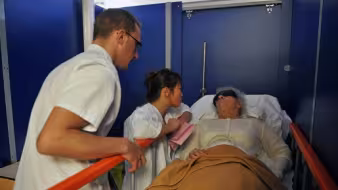 Medical professionals, including an Asian nurse, care for an elderly patient