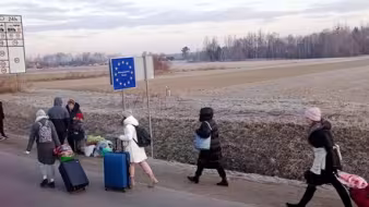 Ukrainians walking on the road with luggage into an EU area 