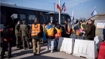Ukrainian refugees and military members stand near a bus in Poland. 