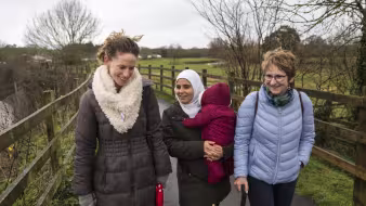 Three women, one in a headscarf and holding a baby, walk in the countryside in Devon, UK