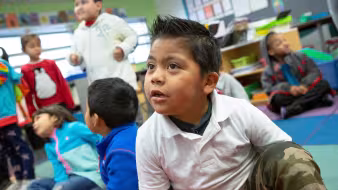 A prekindergarten student sitting on the floor with classmates